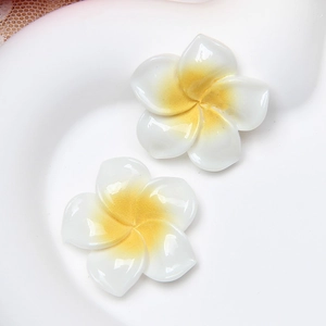 Macro detail of resin frangipani flower charms with white petals and yellow centers
