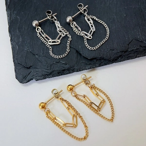 Close-up of gold and silver double chain earrings on a minimalist textured surface