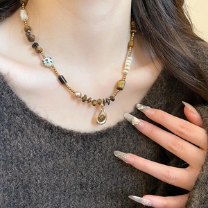 Close-up of tiger eye beaded necklace with teardrop pendant on model wearing brown sweater
