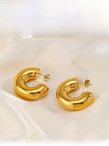 Close-up of chunky 18K gold plated C-shaped hoop earrings on white silk fabric