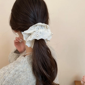Detail of a creamy lace scrunchie with hollow embroidery worn on a ponytail