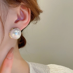 Close-up of a large round faux pearl earring with golden rim on a female model