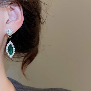 Close-up of luxury water drop earrings featuring green and clear stones on model