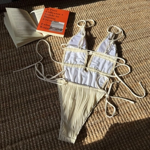 Dettaglio del costume intero avorio plissettato con lacci su un tappeto di paglia