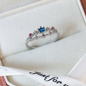 Close-up of a silver ring with blue center stone and colorful zircons in a gift box