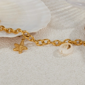 Detail of gold starfish pendant and white shell bead on thick chain bracelet over sand