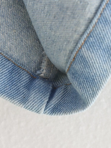 Macro view of light blue denim fabric with orange stitching and edge folding detail