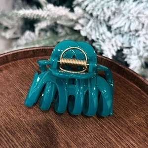 Detail shot of a dark green pumpkin bow hair claw clip on a rustic wooden tray