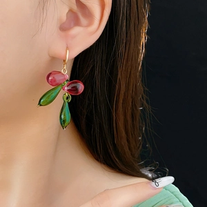 Gros plan de boucles d'oreilles dorées avec perles de verre rouges et gouttes vertes