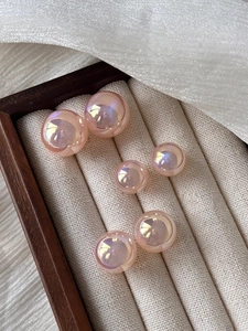 Macro shot of pink iridescent pearl studs in varying sizes on a wooden jewelry box