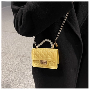 Detail of yellow quilted silicone bag with pearl handle and gold chain on black coat
