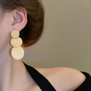 Close-up of triple gold disc earrings with brushed metal texture worn by a model