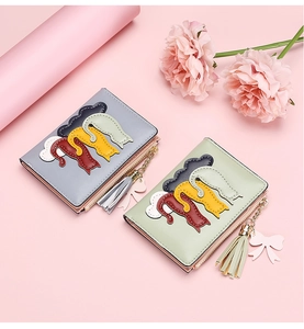 Detail of short bifold cat wallets with tassel charms and bows on warm pink background