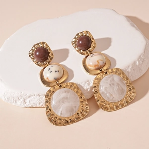 Macro detail of gold-plated geometric earrings with brown and beige resin inlays