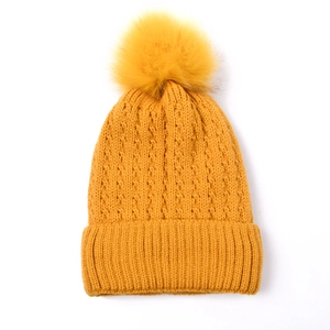 Detailed cable knit texture and faux fur pom-pom on mustard yellow winter beanie