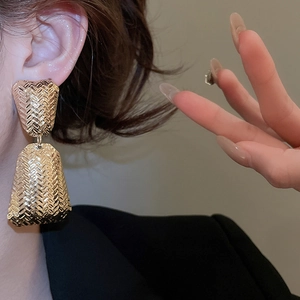 Close-up of a model wearing large golden woven texture metal hoop earrings for women