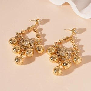 Détail de boucles d'oreilles fleurs dorées avec zircons et perles en métal suspendues