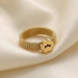 Detail of a gold mesh band ring featuring a delicate paw print charm on champagne silk