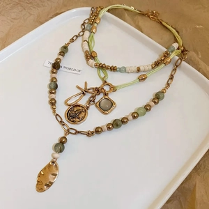 Detail of bohemian layered necklace with green beads, gold coin charms, and square gems