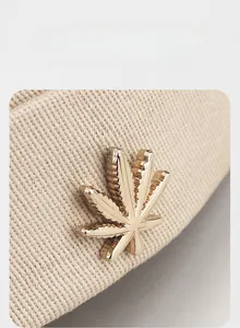 Close-up of beige ribbed knit beanie featuring a detailed gold maple leaf metal badge