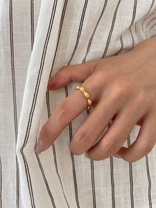 Detail of gold textured bean chain ring worn on index finger over striped shirt