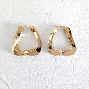 Macro shot of gold twisted geometric triangular earrings on white textured background