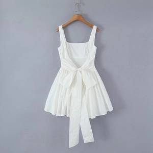 Detail view of a white sleeveless dress featuring a back bow tie and pleated hemline