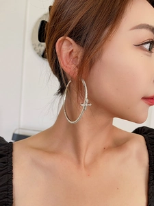 Detail of silver hoop earring with sparkling zircon cross worn by a model