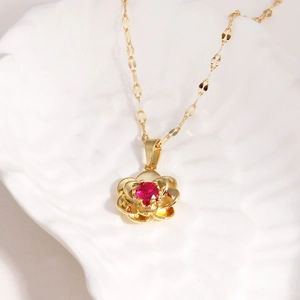Detailed shot of a golden rose pendant with a red ruby centerpiece on a white shell tray