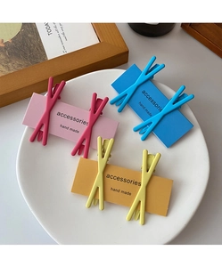 Close-up of three pairs of X-shaped candy color hair clips in pink, blue and yellow