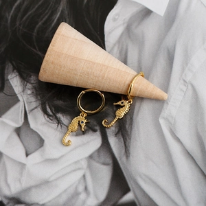 Detailed view of golden seahorse hoop earrings with blue gemstone eyes on display