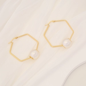 Close-up of golden hexagonal hoop earrings with white pearls on white silk fabric