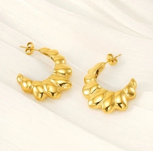 Detailed macro view of 18K gold-plated ribbed C-shape earrings on white silk fabric