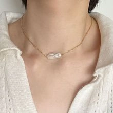 Dettaglio della collana a onde dorate con ciondolo di perla bianca ovale sul collo di una modella