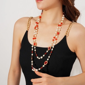 Detailed view of layered pearl necklace with gold chain and red gemstones on model