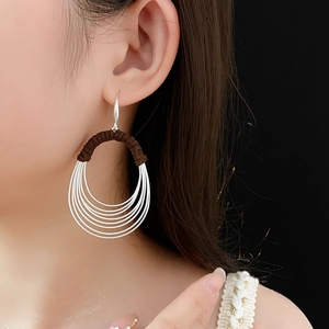 Detail of layered silver metal hoops with brown woven thread wrap worn by a model