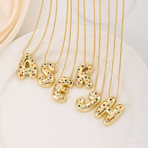 Colorful 3D letter pendants with multicolor zircon stones on gold chains in a ceramic tray