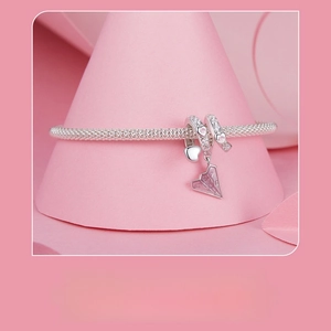 Detailed view of pink paper plane and heart charms on a silver snake chain bracelet