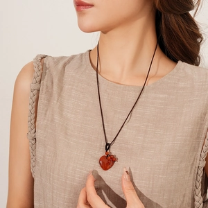 Close-up of a long braided rope necklace featuring a red heart pendant and small beads