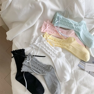 Detail of six pastel ruffled socks with silk bows on a soft white background