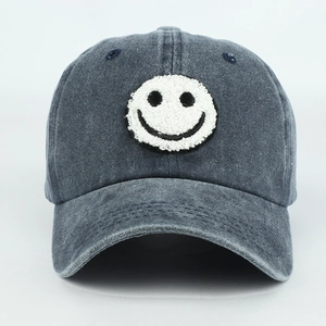 Macro detail of the white chenille smiley face patch on a washed denim baseball cap