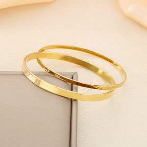 Detail shot of stacked gold flat band bangles with polished mirror finish on luxury fabric