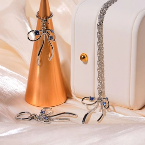 Silver bow necklace and earring set with blue crystals on premium beige silk background