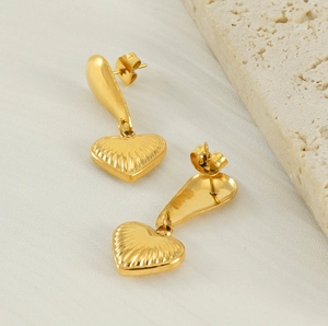 Detailed view of gold heart drop earrings with ribbed texture on white fabric