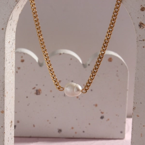 Detailed close-up of a golden chain necklace featuring a white baroque pearl pendant