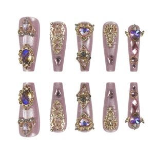 Détail de faux ongles faits main avec gemmes violettes, reliefs dorés et ornements couronne