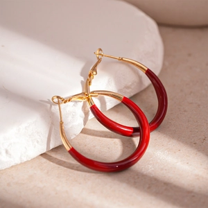Macro detail of red and gold U-shaped enamel hoop earrings on a decorative tray