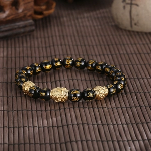 Close-up of black beads bracelet with gold mantra carvings and a buddha head bead