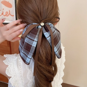 Close-up of blue and brown plaid bow hair tie with a gold bunny button on a low ponytail