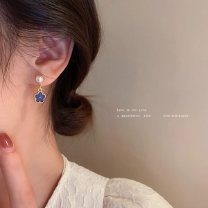 Elegant gold earrings with blue floral drop pendants and white pearls on a model